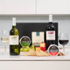 Personalised Fine Wine & Gourmet Cheese Hamper: A selection of two bottles of wine, one white and one red, is displayed alongside two glasses filled with the respective wines. The arrangement includes grapes, various types of cheese, and a box of crackers, all set against a neutral-colored background. Personalised Fine Wine & Gourmet Cheese Hamper: A selection of two bottles of wine, one white and one red, is displayed alongside two glasses filled with the respective wines. The arrangement includes grapes, various types of cheese, and a box of crackers, all set against a neutral-colored background.